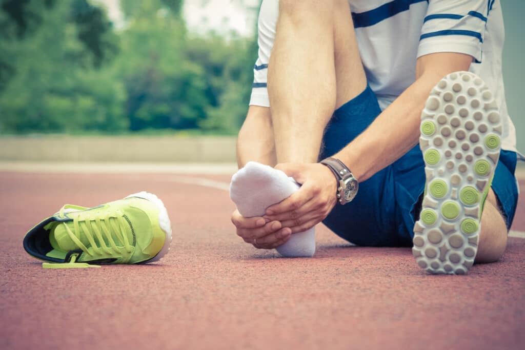 Athlete sitting down with shoe off rubbing his foot due to suspected stress fracture